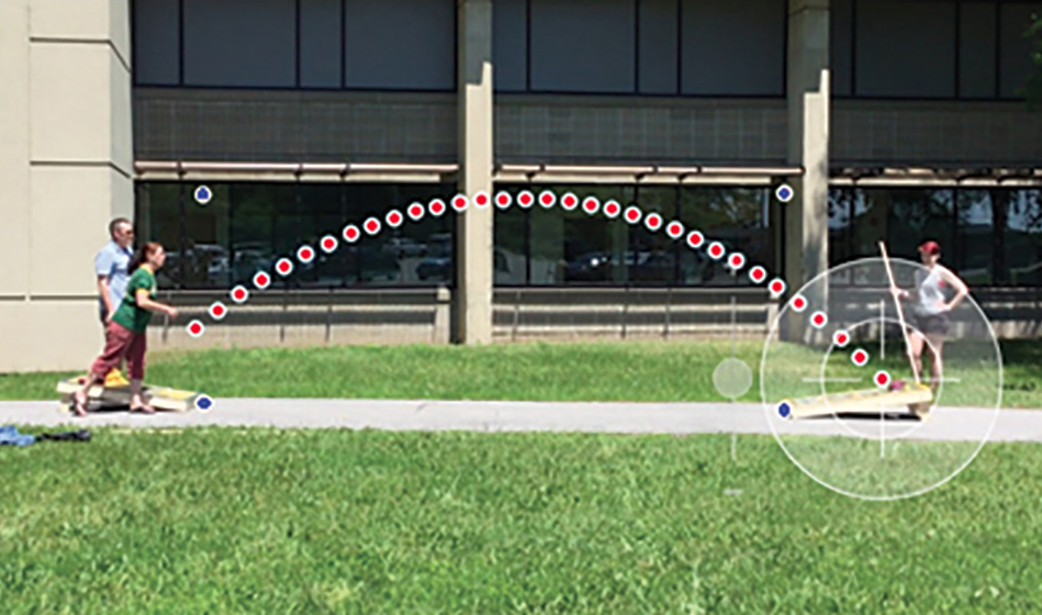 Figure 3 Example of data collection. The trajectory of the corn bag can be seen traced out by the red dots. The white crosshair is placed by the student on the point of interest; the horizontal and vertical coordinates of each dot are recorded to a file. The four calibration points are also shown in blue.